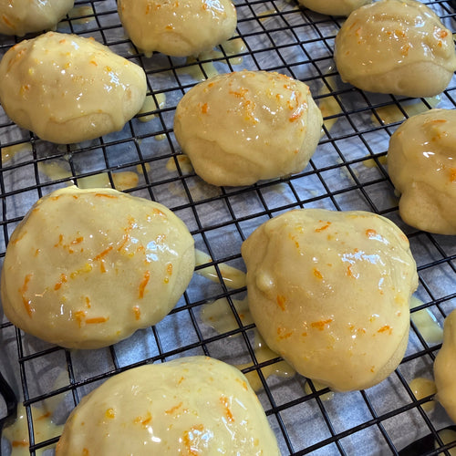 Glossy orange frosted anginetti cookies by sunday tavola sitting on a wire rack. 