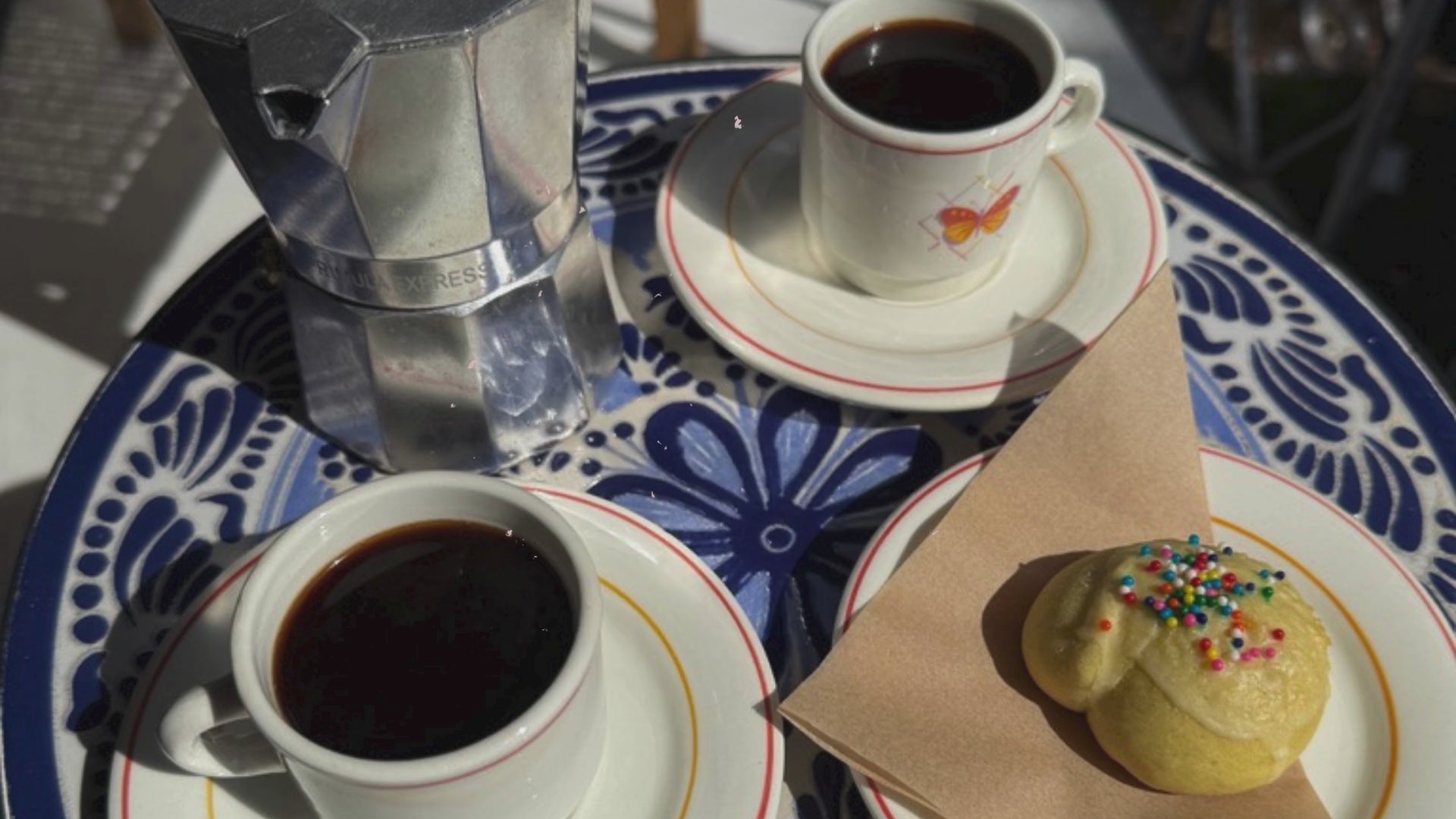 sunday tavola's italian anginetti cookies with coffee and amaro on a blue table sitting on a patio in the sunlight. 
