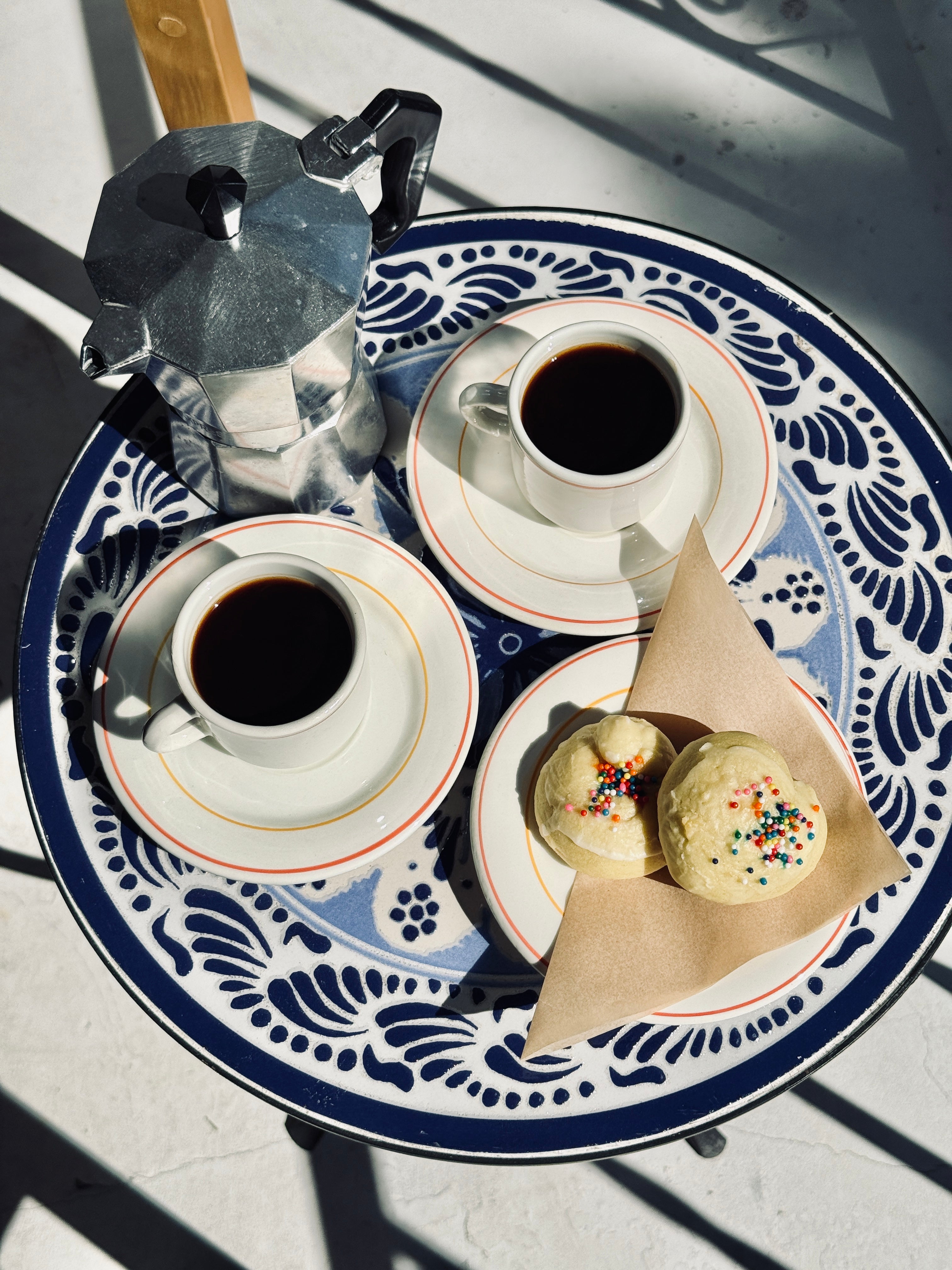 Two cups of coffee and two Italian cookies on a decorative table with a blue and white pattern.