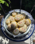 sunday tavola anginetti—italian wedding cookies with rainbow sprinkles and lemon icing on a decorative plate sitting in the sunlight